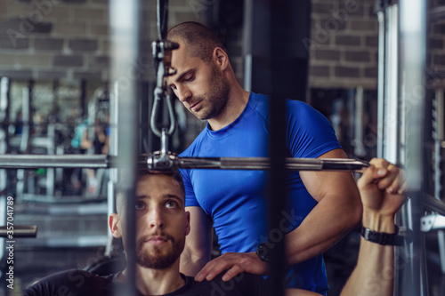 Muscular young man is exercising in the gym with his personal fitness instructor.