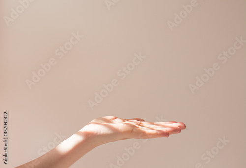  Female hand holds copy space and some object on a white background with beautiful shadows. Layout and frame in the sun