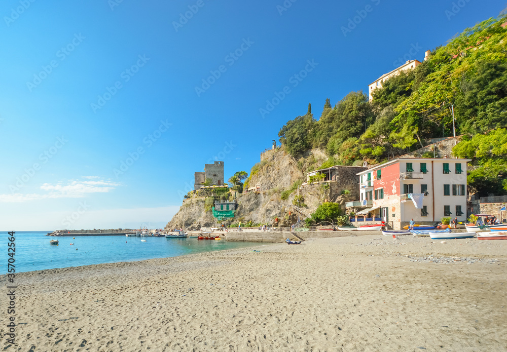 The ruins of the Aurora Tower Castle at Monterosso al Mare rise above the sandy beach and coast in Cinque Terre Italy on the Ligurian Coast