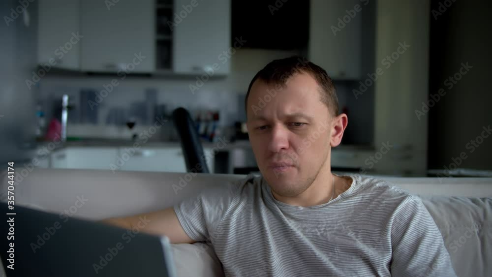 A man works on a laptop while sitting at home on a sofa, remote work A man works on a laptop while sitting at home on a sofa, remote work