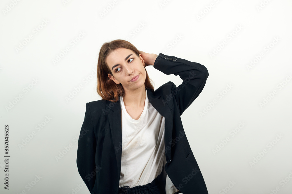 Stress or a headache grimacing in pain holds the back of neck indicating location. Fatigue during workaholism labor. Young attractive woman with brown hair in a light t-shirt and black jacket Stress or a headache grimacing in pain holds the back of neck indicating location. Fatigue during workaholism labor. Young attractive woman with brown hair in a light t-shirt and black jacket