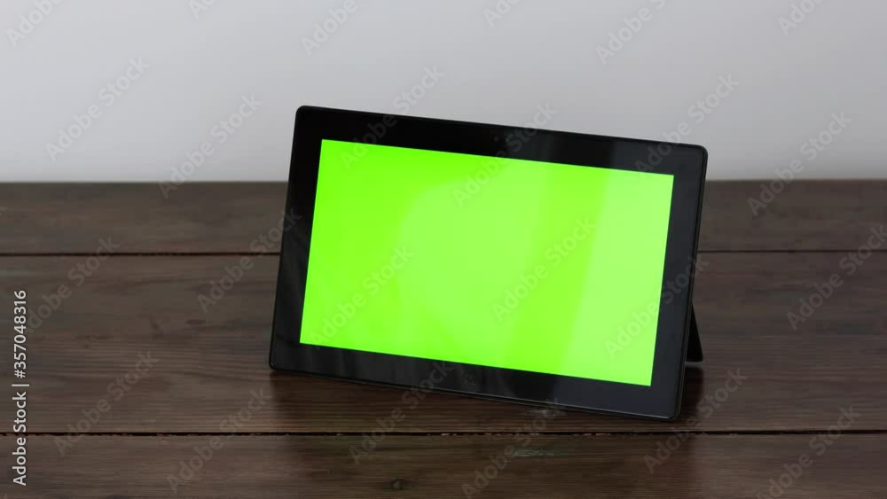 A tablet with a green screen on a wooden table, makes a doubletap with a finger. A tablet with a green screen on a wooden table, makes a doubletap with a finger.
