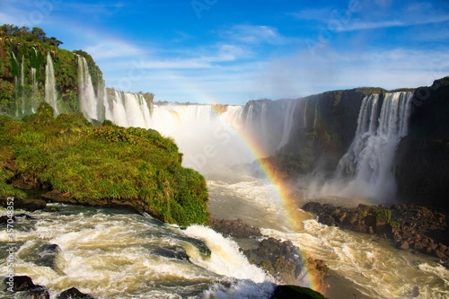 Cacheira, cataratas do Iguaçu. Em Foz do Iguaçu, Paraná, Brasil. Céu azul, dia ensolarado, um arco íris é formado em frente as cataratas. Pode-se ver as rochas e natureza do local. Ponto turístico.