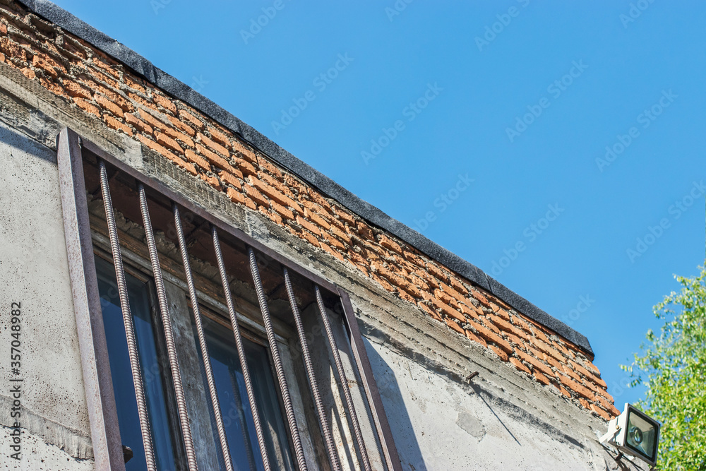 Part of an old industrial building with windows on which there are metal bars. Blue sky and bright sunlight on a hot summer day. Walks around the city in the summer.
