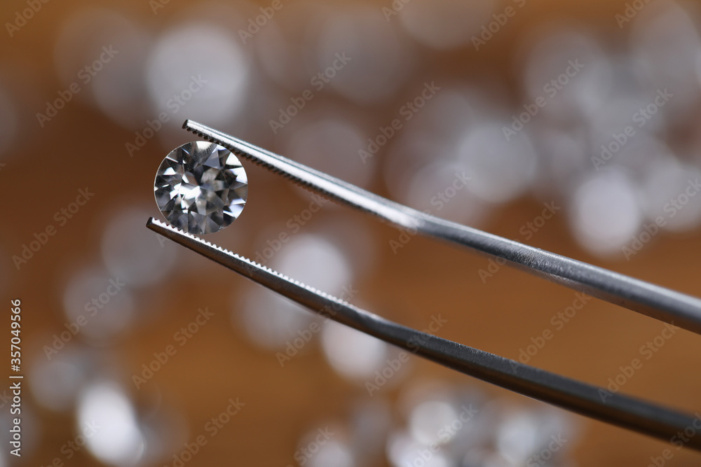 Close-up of bright shining crystal. Macro shot of fancy round shaped white diamond in workers tweezers. Carat size. Jeweler checking polished brilliant. Precious stone concept Close-up of bright shining crystal. Macro shot of fancy round shaped white diamond in workers tweezers. Carat size. Jeweler checking polished brilliant. Precious stone concept