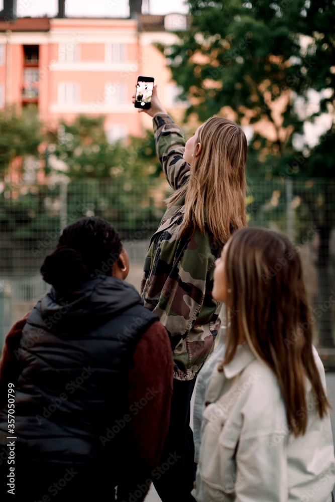 Teenage girl taking selfie with friends through smart phone in city Teenage girl taking selfie with friends through smart phone in city