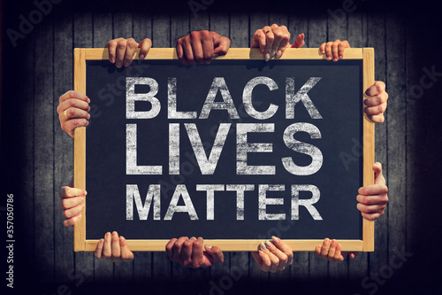 A lot of hand are holding a banner with text BLACK LIVES MATTER on dark background. Different people express one common opinion Black lives matter