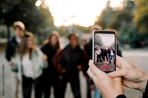 Cropped hands of woman with smart phone filming teenagers dancing on street in city