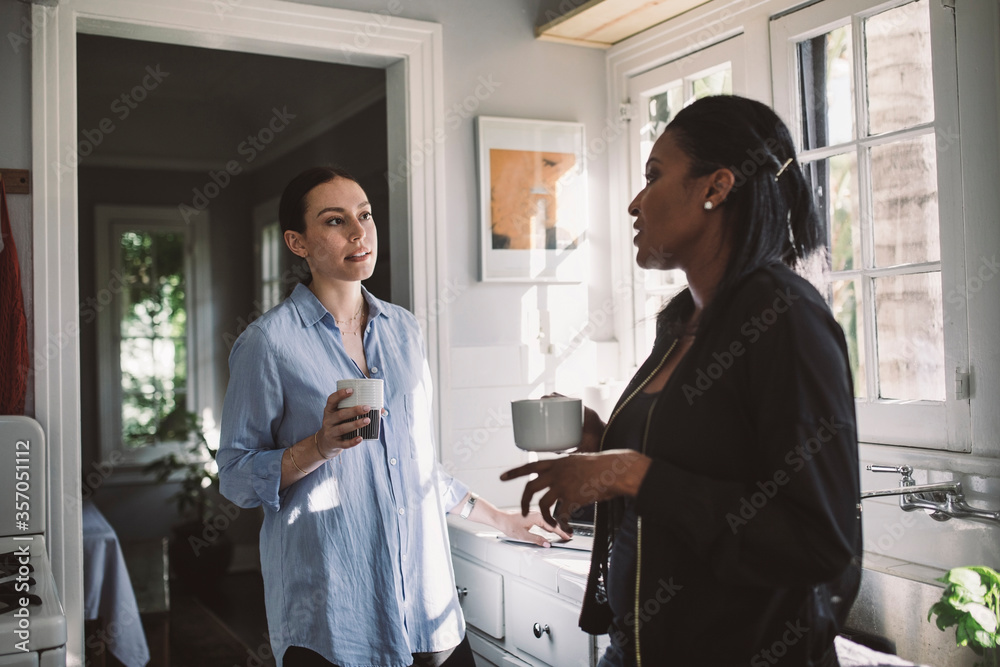 Female designers discussing while standing by kitchen counter at home Female designers discussing while standing by kitchen counter at home