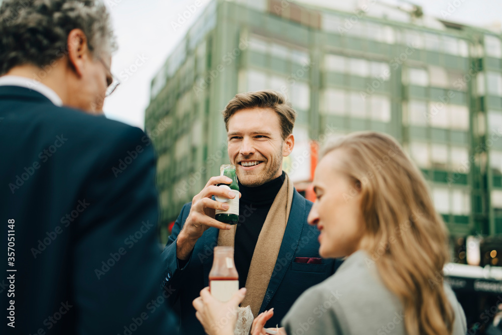 Smiling male entrepreneur with drink looking at coworkers in city Smiling male entrepreneur with drink looking at coworkers in city