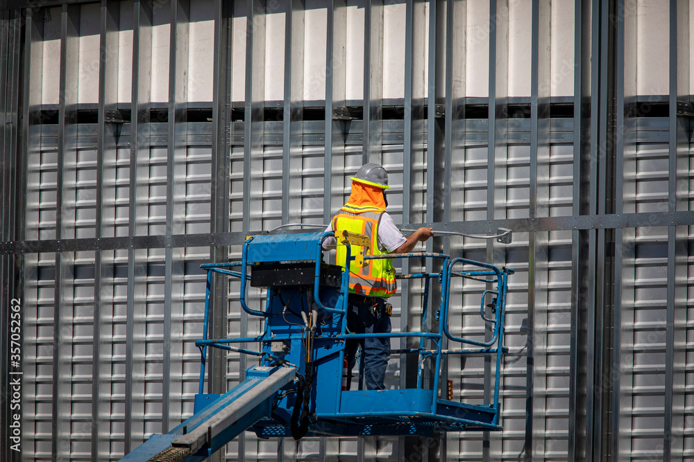 Construction worker on blue man lift working on metal prefab building