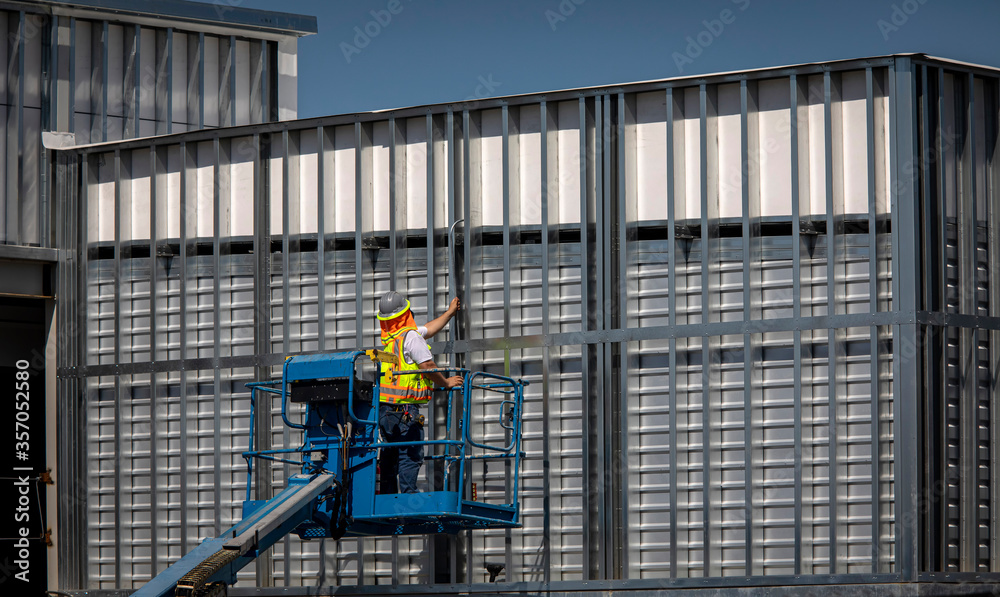 Construction worker on blue man lift working on metal prefab building