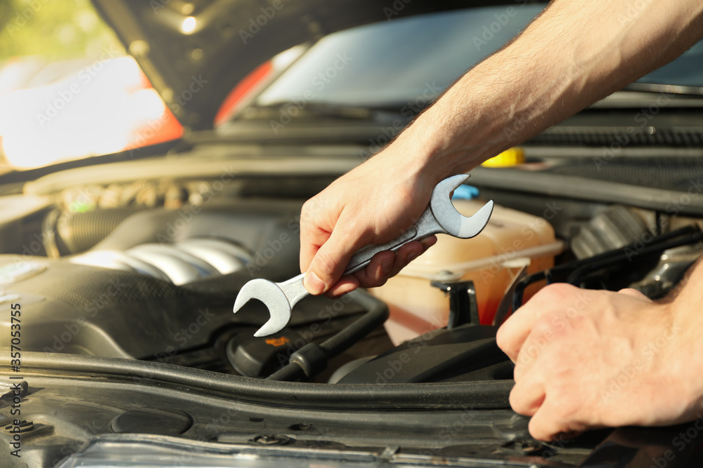 A man holds a wrench over a car engine. Car inspection