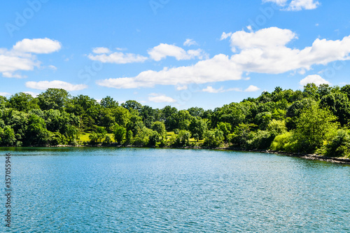 Landscape of lake and woods with blue sky and puffy clouds