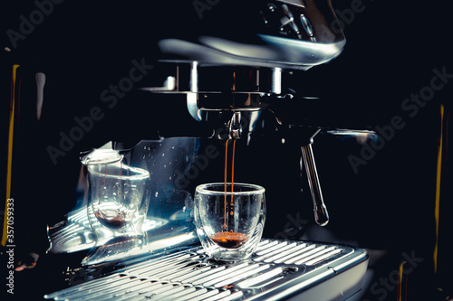 Dark coffee drops dripping in a transparent glass espresso cup on a manual espresso machine with copy space, close up