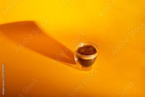 Freshly brewed creamy espresso in a glass coffee cup isolated on yellow background, close up with copy space