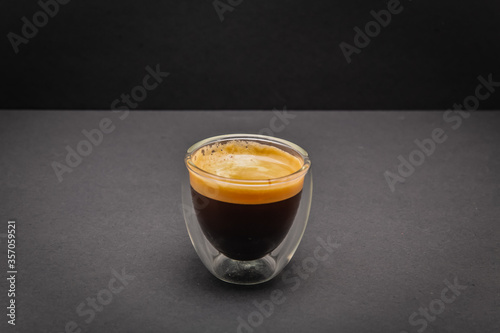 Freshly brewed creamy espresso in a glass coffee cup isolated on grey and black background, close up with copy space