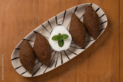 fried kibbeh yogurt sauce served on a white plate. top view photo