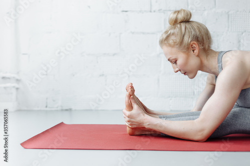 woman in triang mukhaikapada pashchimottanasana yoga position. Young attractive woman practicing yoga, working out, wearing sportswear, pants and top, indoor full length, yoga studio photo