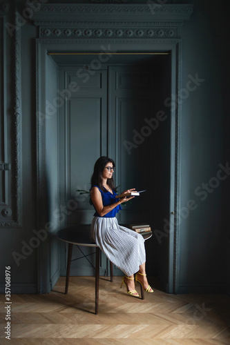 Woman in elegant clothes sitting on table in modern interior