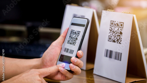 Closeup of a hand holding phone and scanning qr code. Man hand paying with qr code. Customer hand making payment through smart phone and scan code. Selective focus. photo