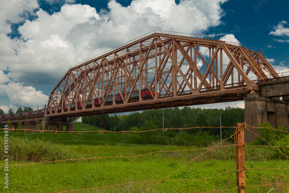 Suburban train rides on a high old iron bridge with concrete piers