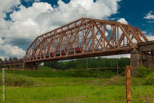 Suburban train rides on a high old iron bridge with concrete piers