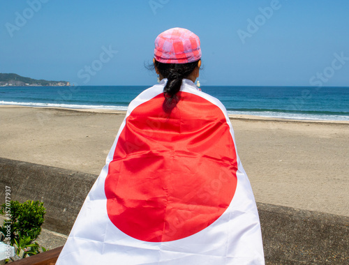 Japanese lady with Japan flag over her at the beach with the Pacific Ocean in the background, near to Shidashita the Olympic surf venue for surfing. Chiba photo