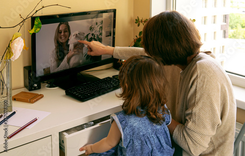 A young woman with a child remotely communicates with her friend. Mom introduces the daughter to the pet of friend via video link. Staying in touch during Covid concept.