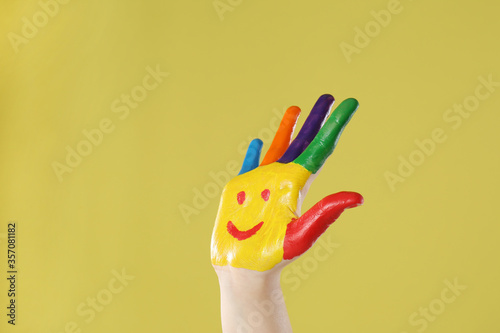 Kid with smiling face drawn on palm against yellow background, closeup