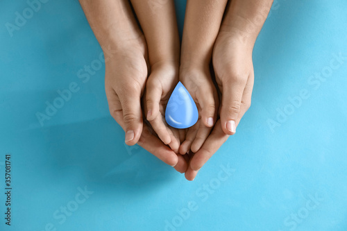 Mother and her child holding water drop on blue background, top view. Ecology protection