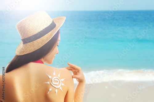 Young woman with sun protection cream on her back at beach  space for text