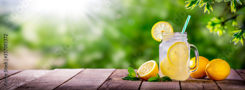 
Refreshing Glass Of Lemonade On Wooden Table With Lemons, Tea Leaves And Sunlight
