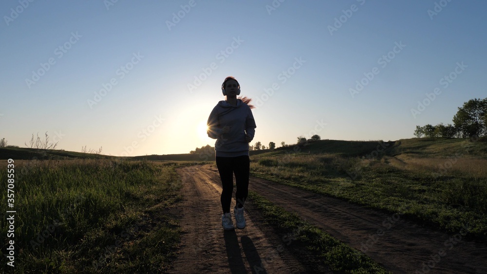 sports for burning calories and losing weight. young woman is training in summer in park at dawn in headphones with music. Free beautiful girl is engaged in fitness. Jogger girl breathes fresh air