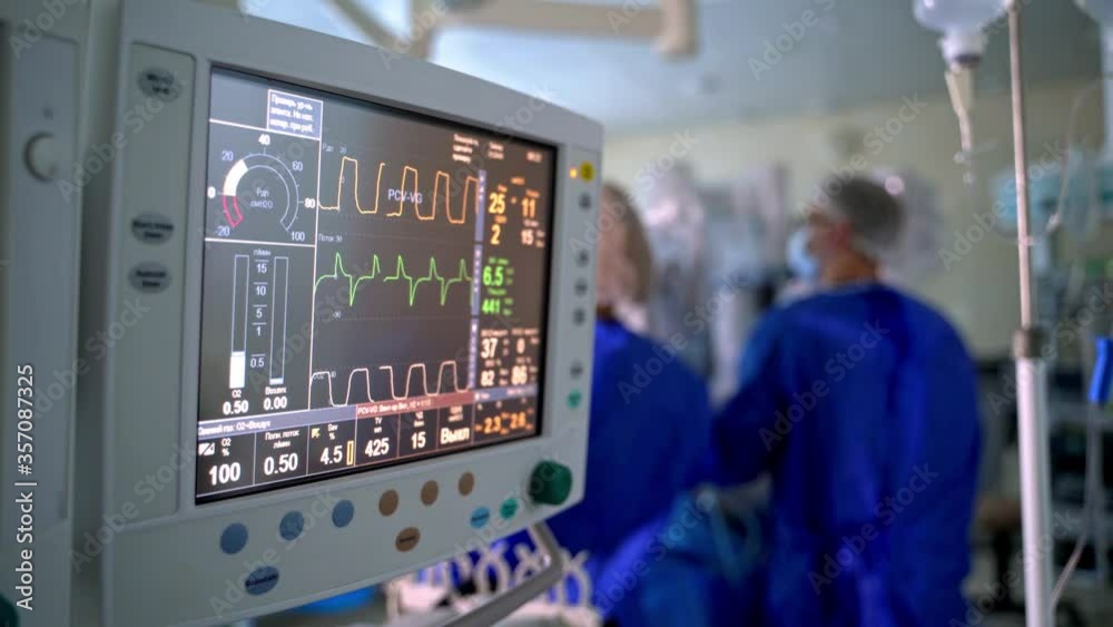 Hospital monitor in the operating room. Screen shows vital signs of a patient on the background of surgical procedure. Teamwork of doctors.
