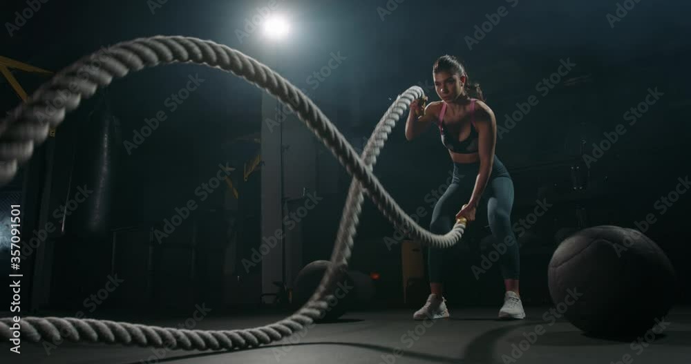 Active dedicated motivated female athlete training in gym with battle ropes, determined confident girl enjoying bodybuilding achieving goals with healthy lifestyle 4k footage