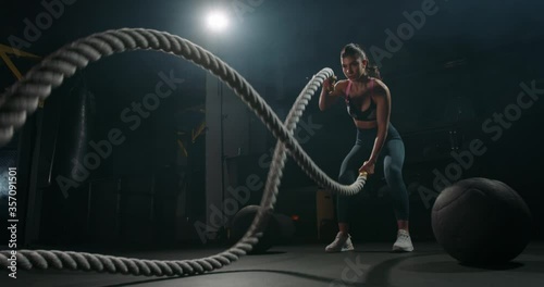 Active dedicated motivated female athlete training in gym with battle ropes, determined confident girl enjoying bodybuilding achieving goals with healthy lifestyle 4k footage photo