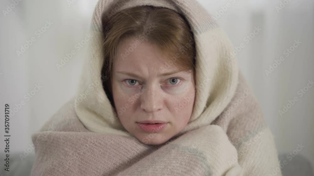 Close-up of ill beautiful woman shivering. Portrait of Caucasian millennial girl wrapped in blanket suffering from cold and flu. Covid-19 pandemic, illness, health care, medicine. Close-up of ill beautiful woman shivering. Portrait of Caucasian millennial girl wrapped in blanket suffering from cold and flu. Covid-19 pandemic, illness, health care, medicine.