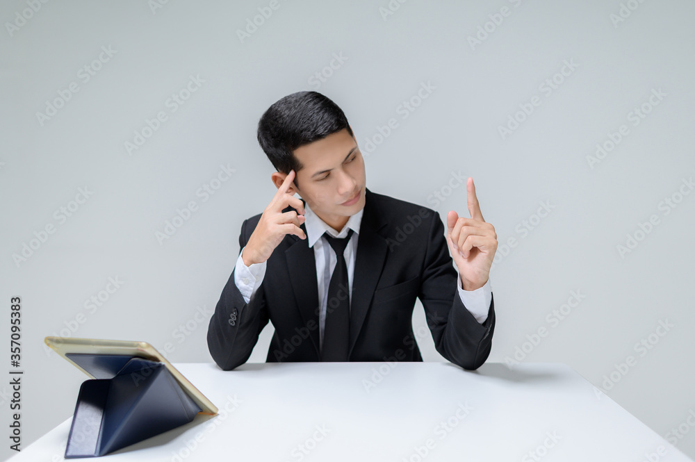 Portrait of handsome young businessman sit think and pointing of look a finger at a desk . The person sitting at the desk isolated studio shot. Portrait of handsome young businessman sit think and pointing of look a finger at a desk . The person sitting at the desk isolated studio shot.
