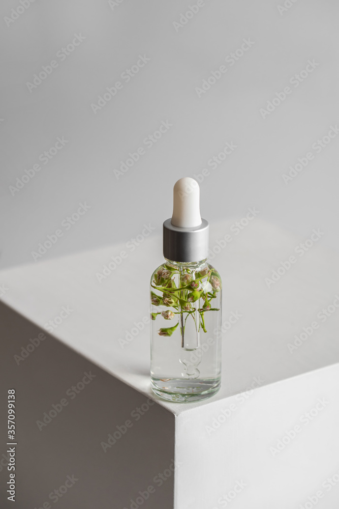 Glass transparent bottle with serum and flowers with a pipette for skin care on a light background. Cosmetics with natural ingredients. The concept of health and beauty. minimalism Glass transparent bottle with serum and flowers with a pipette for skin care on a light background. Cosmetics with natural ingredients. The concept of health and beauty. minimalism