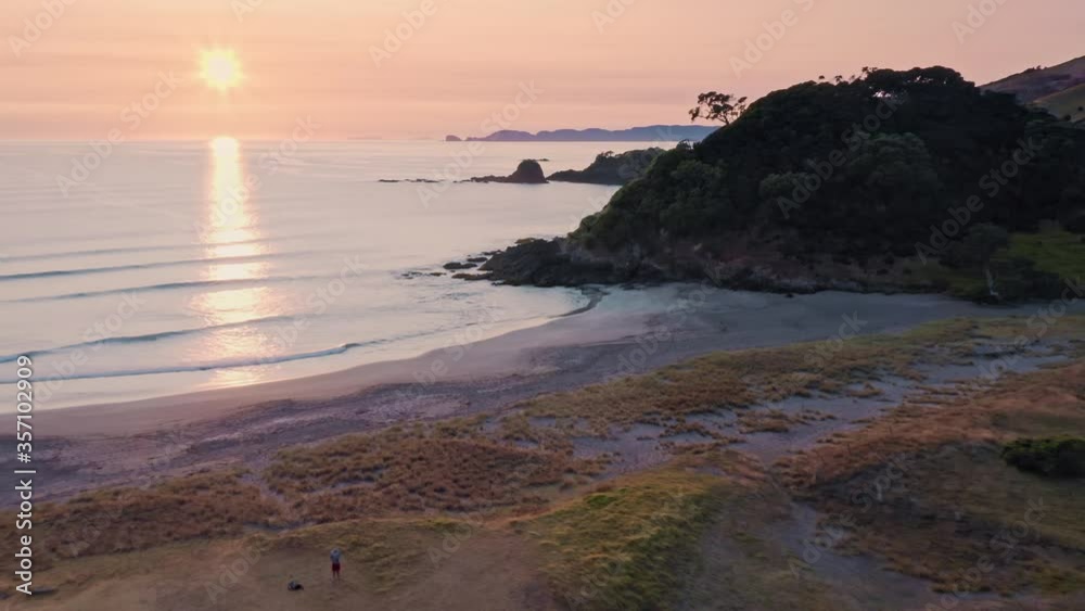 Aerial: Flying over Beach and ocean waves at sunrise. Elliot Bay, Northland, New Zealand