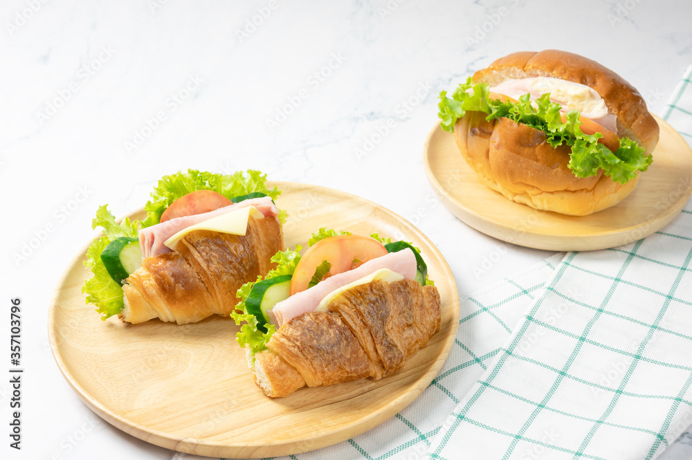 Delicious croissants sandwichs with fresh Ham, cheese, tomato, cucumber, lettuce and Sub sandwich with fresh salad, Ham , cheese served on round wooden plate. white background. Delicious croissants sandwichs with fresh Ham, cheese, tomato, cucumber, lettuce and Sub sandwich with fresh salad, Ham , cheese served on round wooden plate. white background.