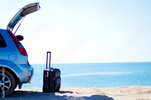 travel suitcase at the open trunk of a car on the beach by the sea