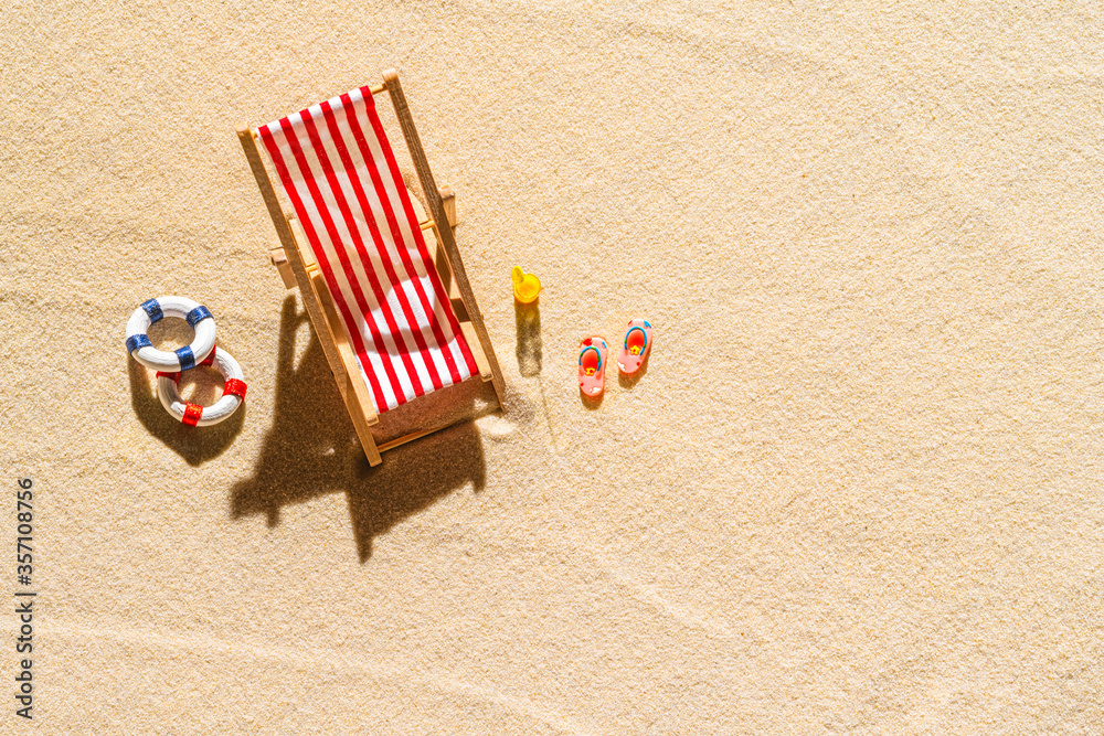 Aerial view of one deck chair, sunbed, lounge, glass of orange juice, flip flops, Lifebuoy on sandy beach. Summer and travel concept. Minimalism Aerial view of one deck chair, sunbed, lounge, glass of orange juice, flip flops, Lifebuoy on sandy beach. Summer and travel concept. Minimalism