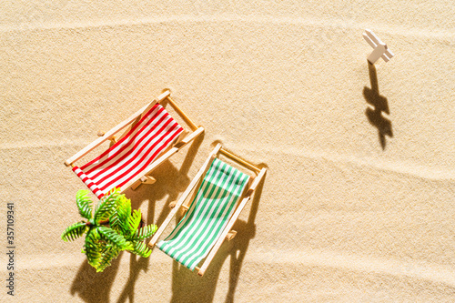 Aerial view of two deck chair, sunbed, lounge, palm tree on sandy beach. Summer and travel concept. Minimalism