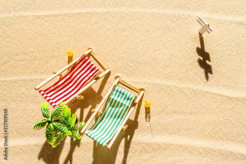 Aerial view of two deck chair, sunbed, lounge, glass of orange juice, palm tree on sandy beach. Summer and travel concept. Minimalism