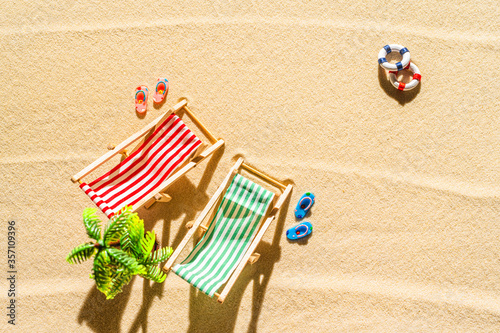 Aerial view of two deck chair, sunbed, lounge, flip flops, Lifebuoy, palm tree on sandy beach. Summer and travel concept. Minimalism