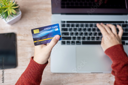 Fototapeta Naklejka Na Ścianę i Meble -  woman wearing sweater holding credit card and using laptop for online shopping while making order at home office. business, lifestyle, technology, ecommerce, digital banking and online payment concept