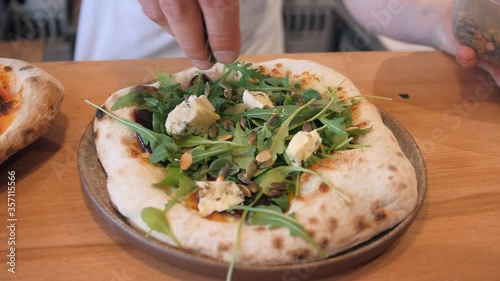 experienced chef sprinkles dark seeds on cooked pizza with arugula and Dor blue cheese preparing order close view photo