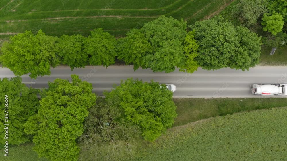 Rising up drone shot with the view vertical directed onto a road while a concrete mixer vehicle is passing by the street.